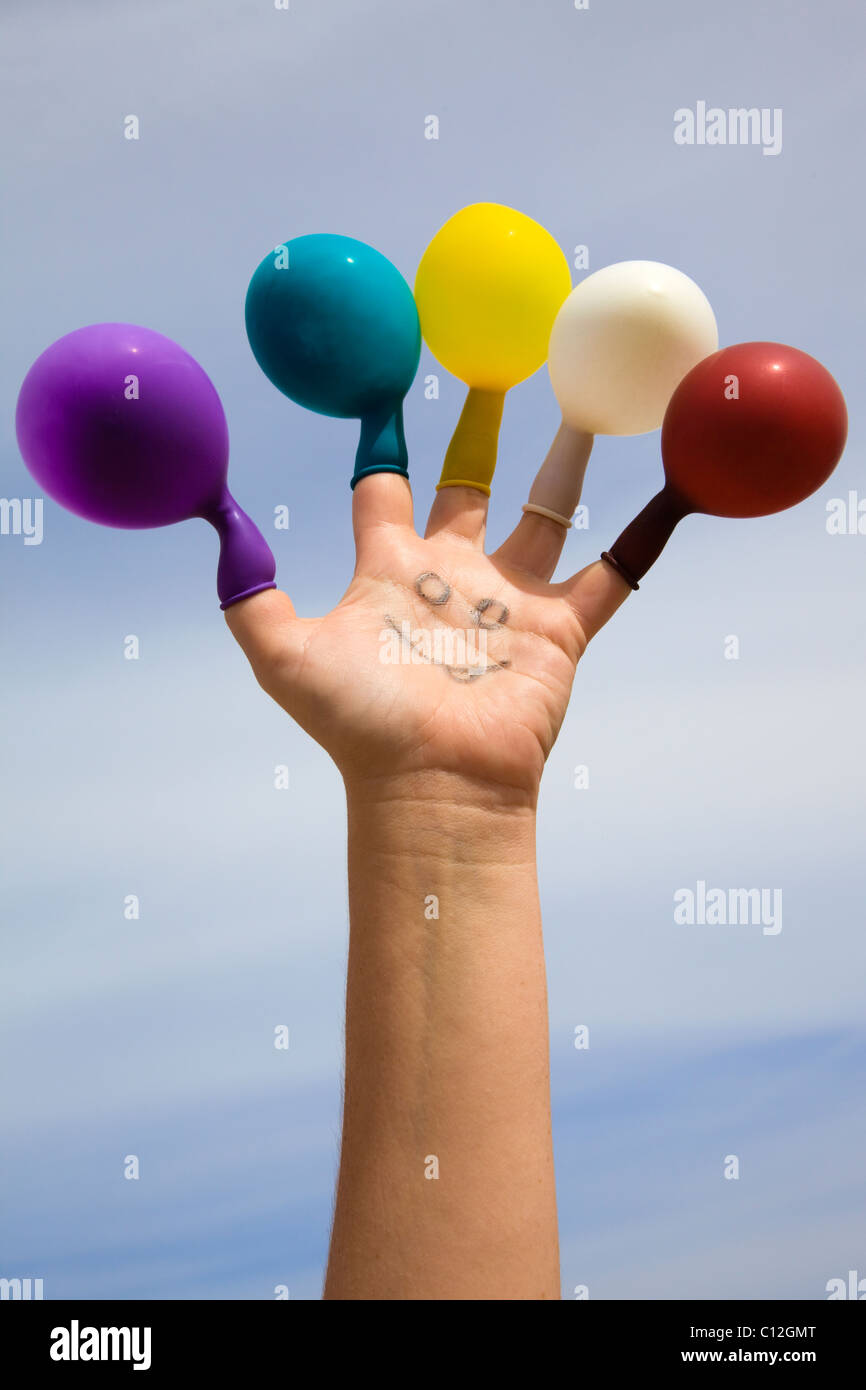 Face drawn on a hand with colored balloons on the fingers Stock Photo