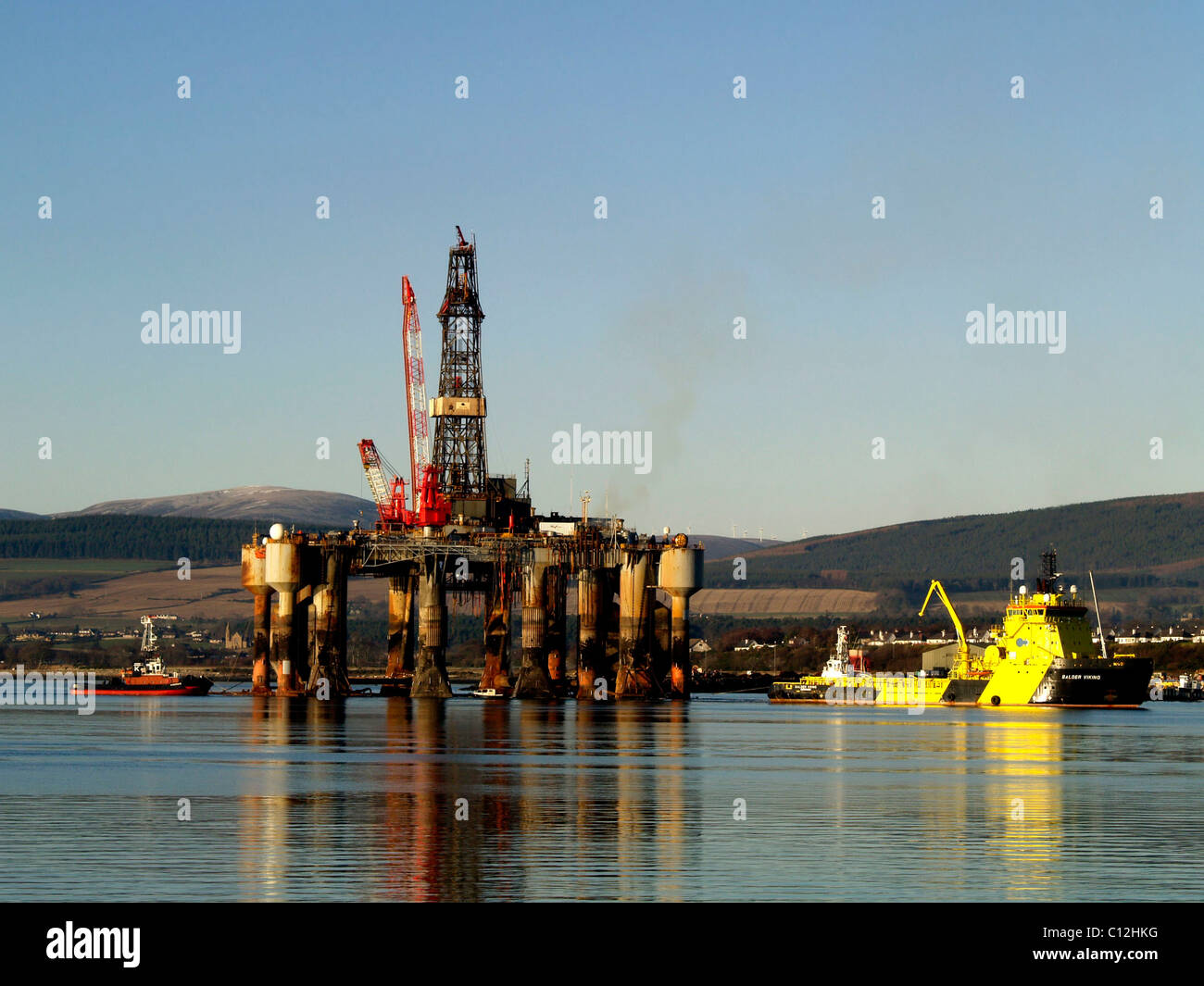 An anchor handling vessel and tug maneuver a semi-submersible oil rig alongside the dock at Invergordon in the Cromarty Firth. Stock Photo
