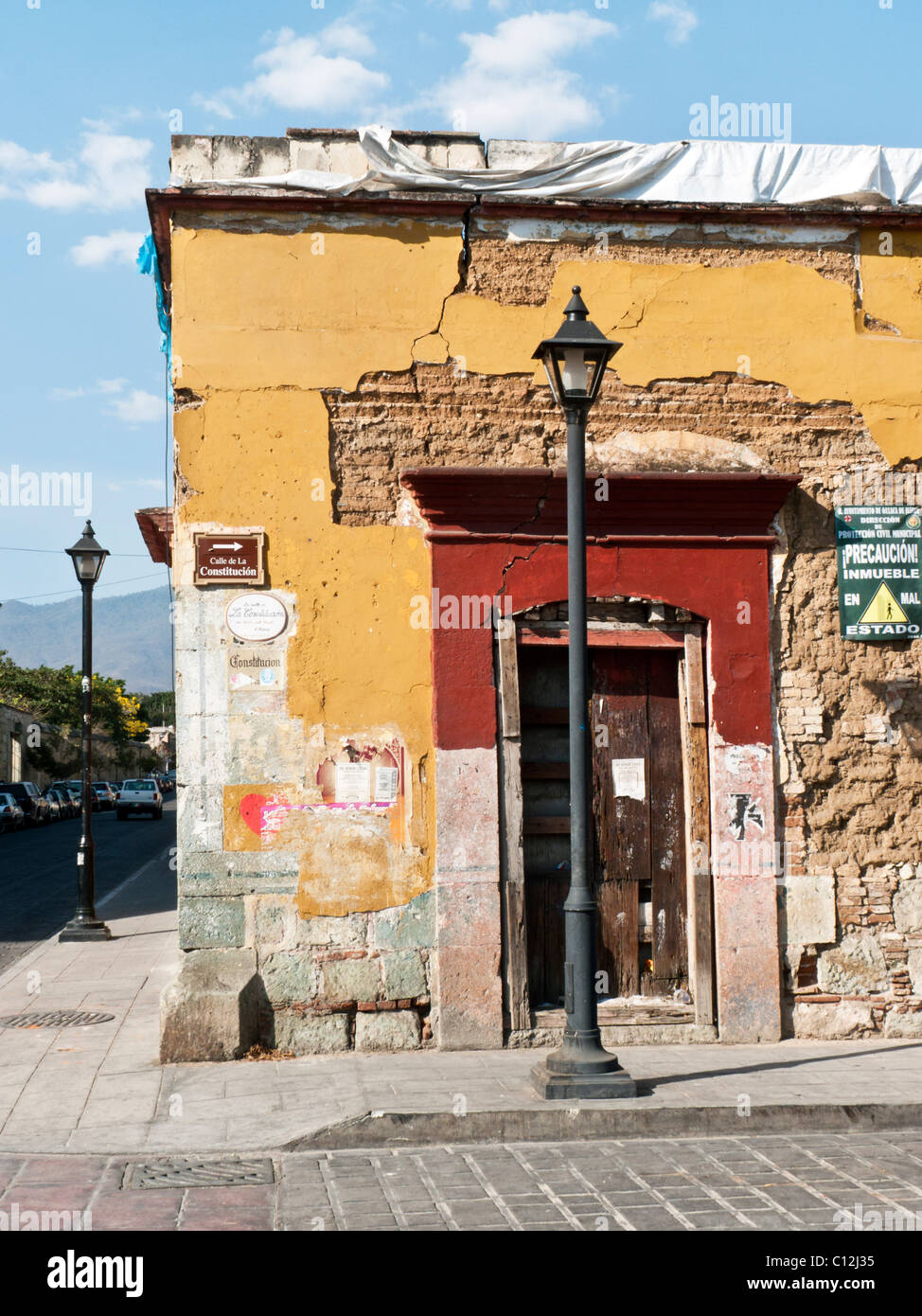 tumbledown old building for sale with yellow plaster clinging to adobe walls & posted public notice of safety hazard Oaxaca Stock Photo