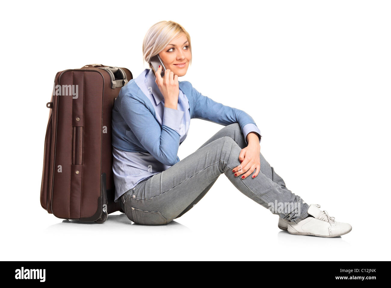 A tourist girl seated next to a suitcase talking on mobile phone Stock Photo