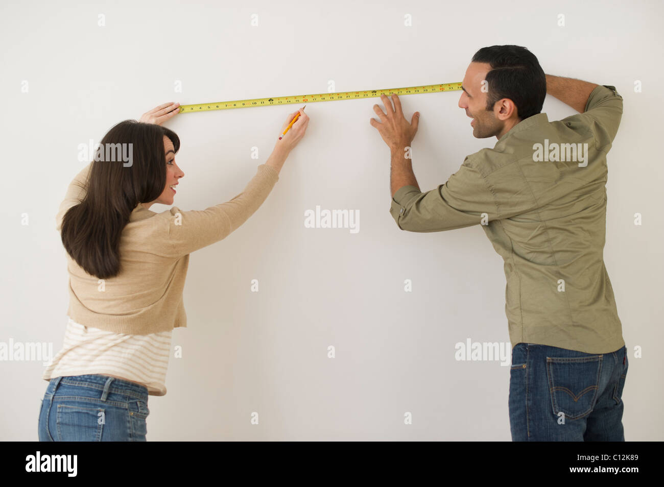 Couple measuring wall, studio shot Stock Photo
