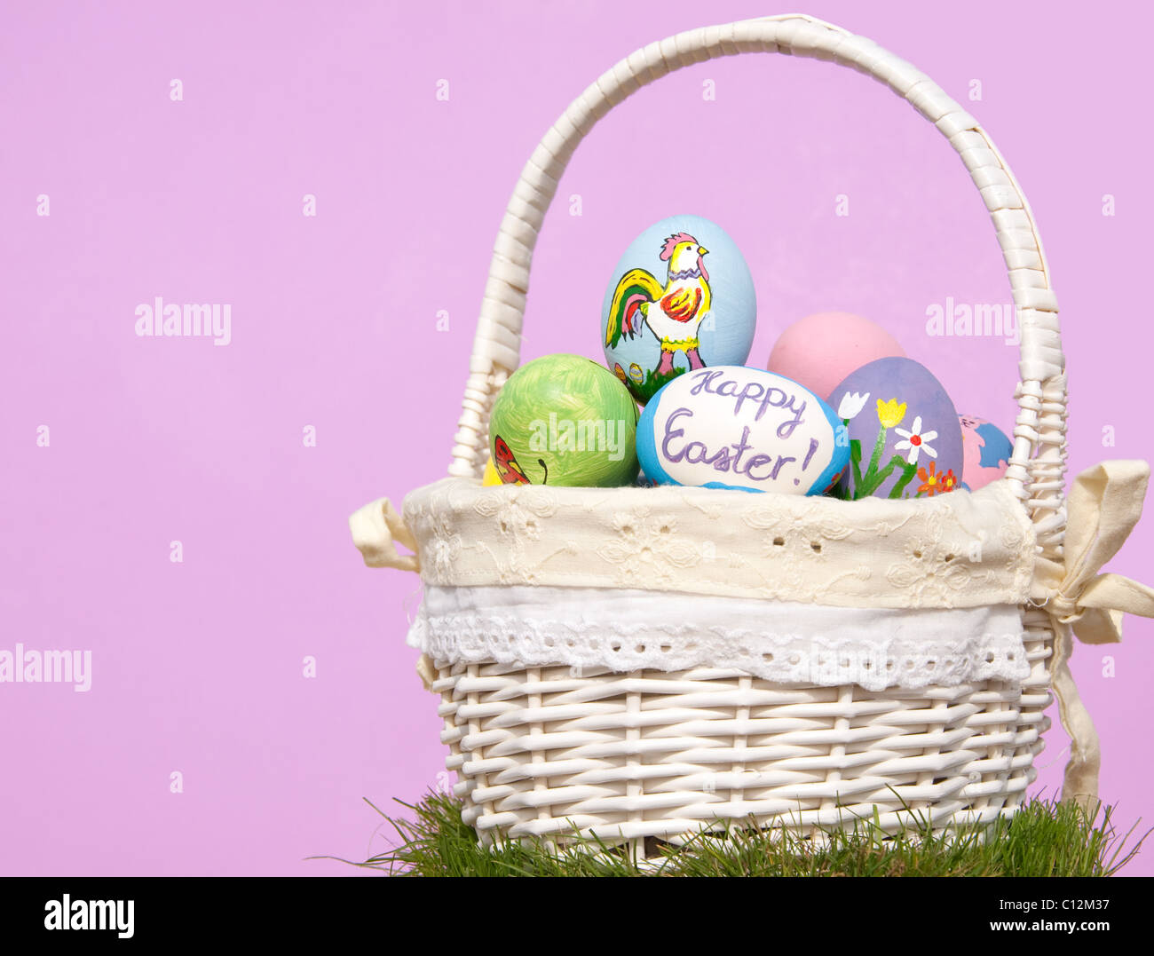Basketful of colorful Easter eggs against purple background, with copy space Stock Photo
