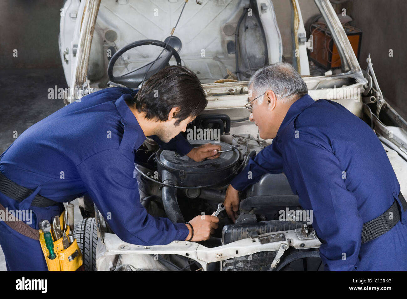 Auto mechanic with an apprentice repairing a car in a garage Stock