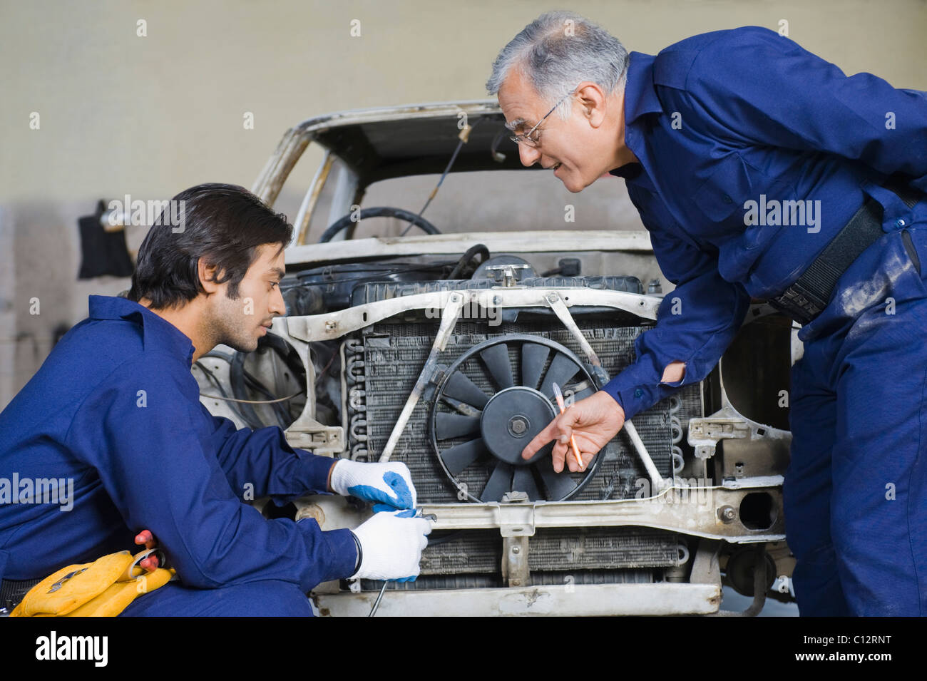 Auto mechanic with an apprentice repairing a car in a garage Stock