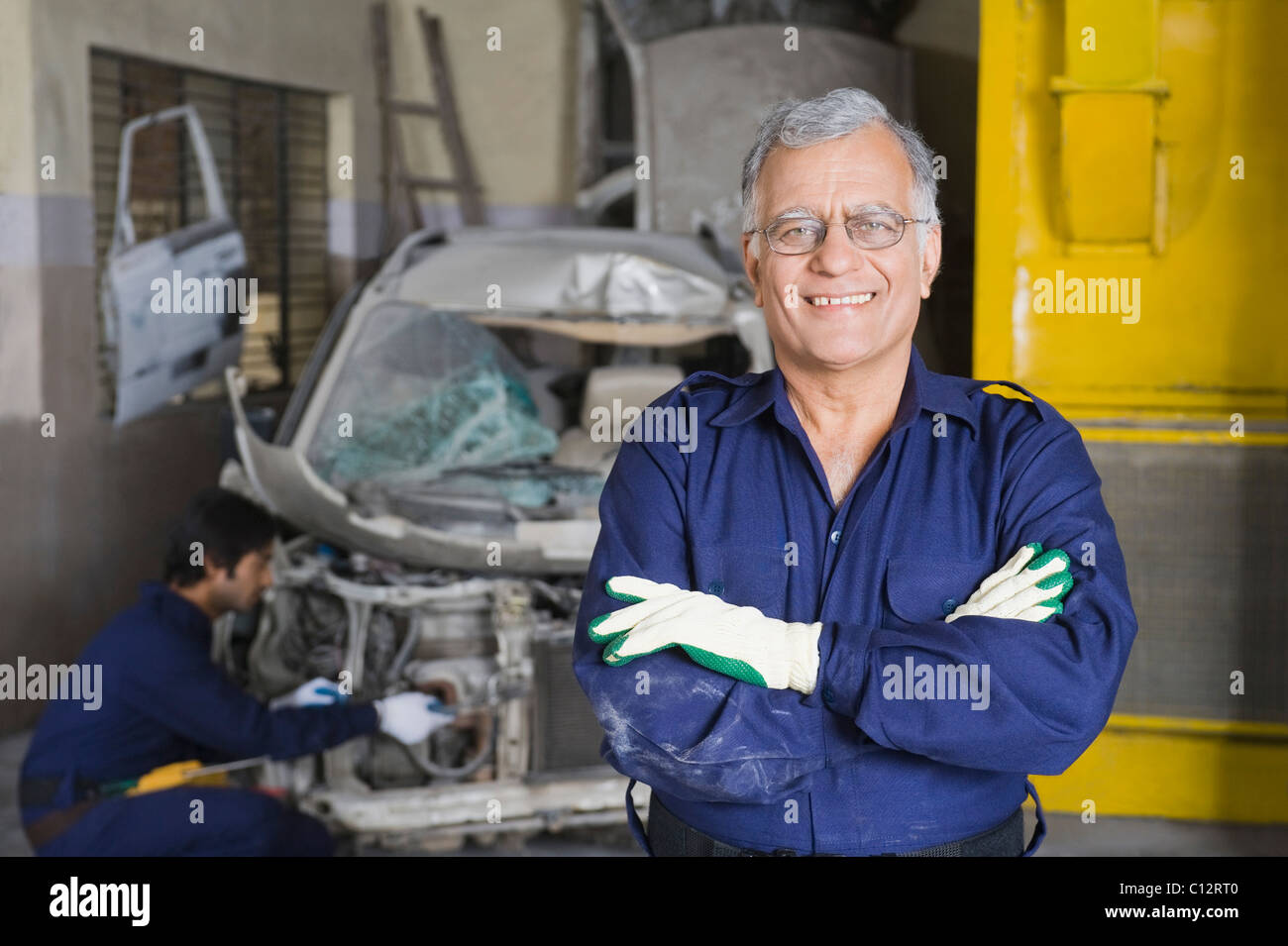 Portrait of an auto mechanic smiling with an apprentice repairing a car in the background Stock Photo