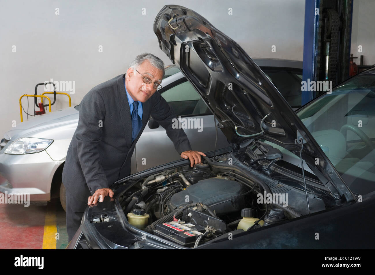 Businessman leaning on a car in a workshop Stock Photo