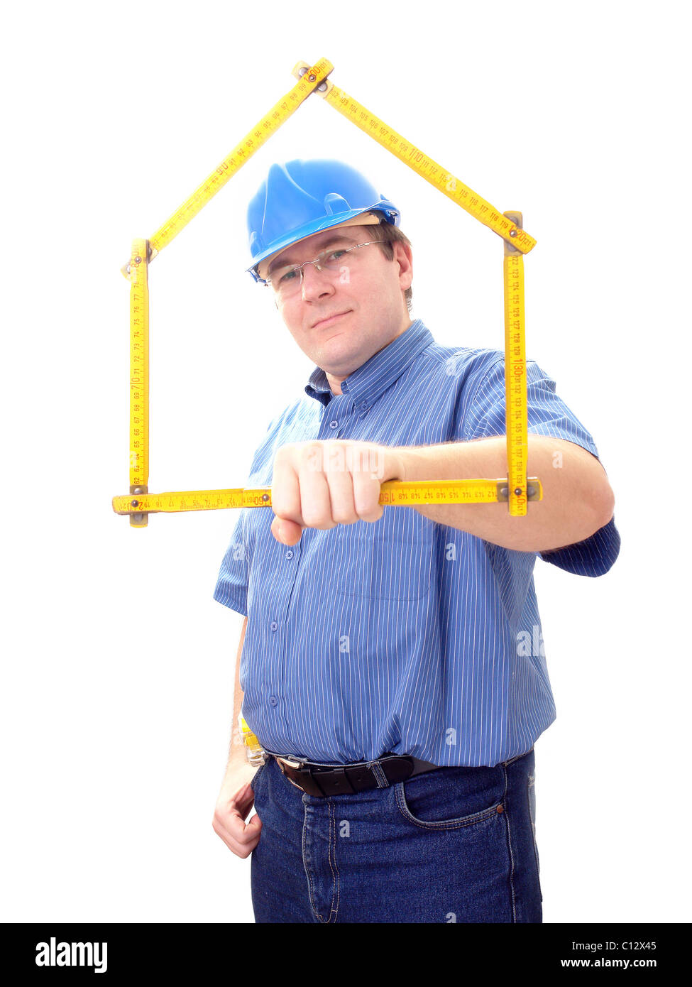Construction site manager wearing blue helmet framing his face with yellow wooden folding rule in form of house over white Stock Photo
