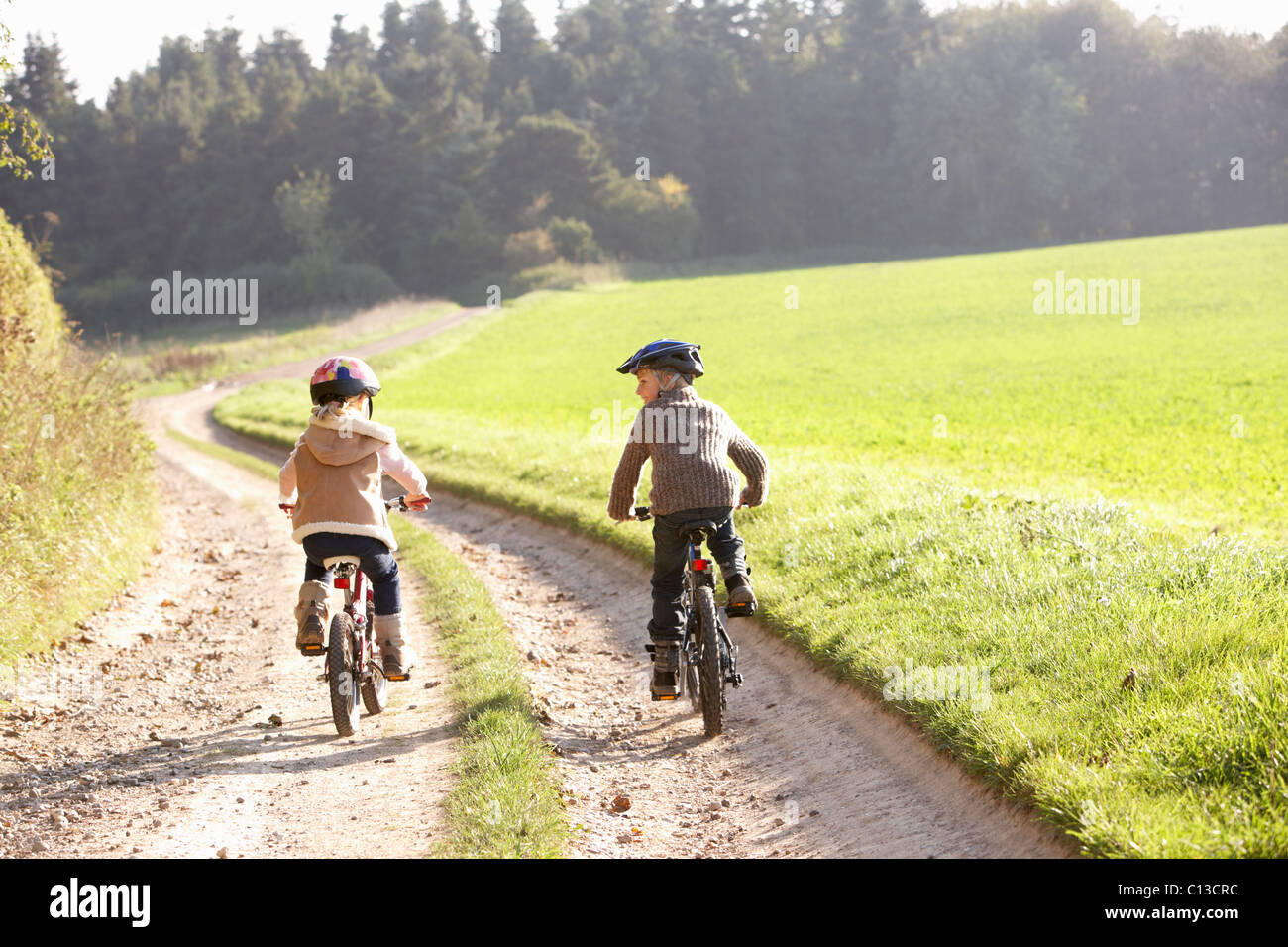Two young children ride bicycles in park Stock Photo
