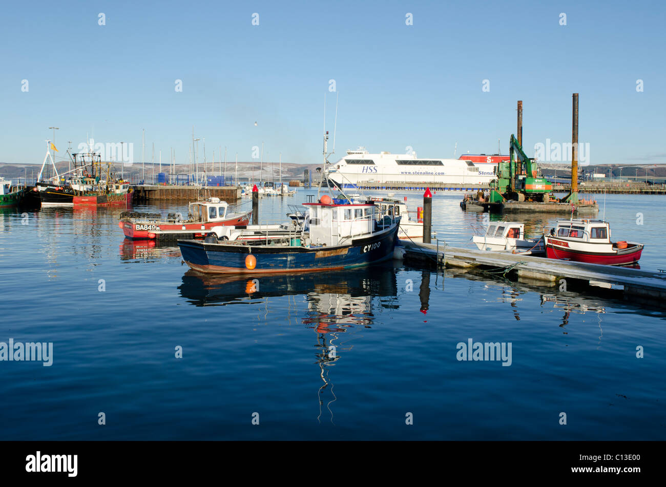 Collection of small working boats moored in Stranraer Harbour with Larne Ferry in background Stock Photo