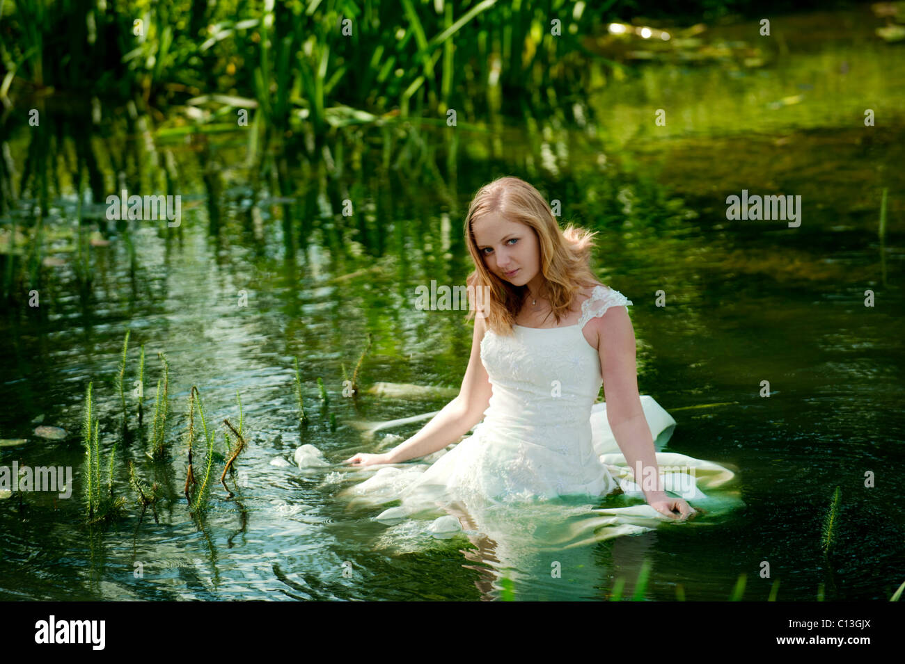 woman lady walking into lake water up to her waist in long wedding dress  with lily pads and reeds trash the dress Stock Photo - Alamy