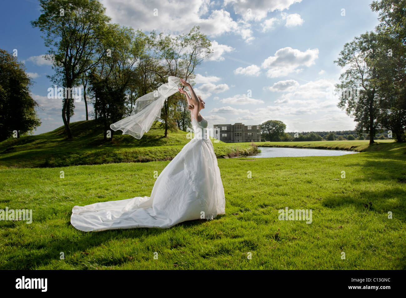 bride walking across grass holding veil blowing in wind above head Stock Photo