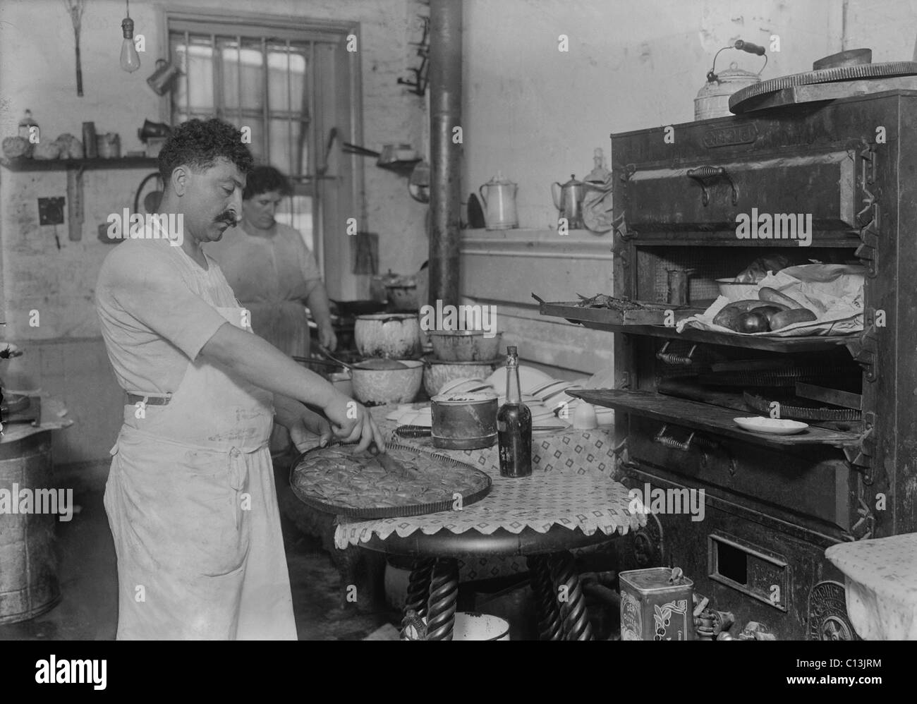 Lebanese-Syrian immigrant pastry cook cutting into a phyllo dough sweet made in the rustic kitchen of in a New York City ethnic Stock Photo