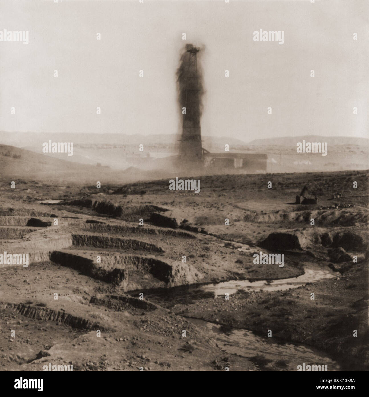 An oil gusher spouting in the Kirkuk District of Iraq, creating a stream of oil seen in the photo foreground. 1932-33. Stream of oil in foreground. Stock Photo