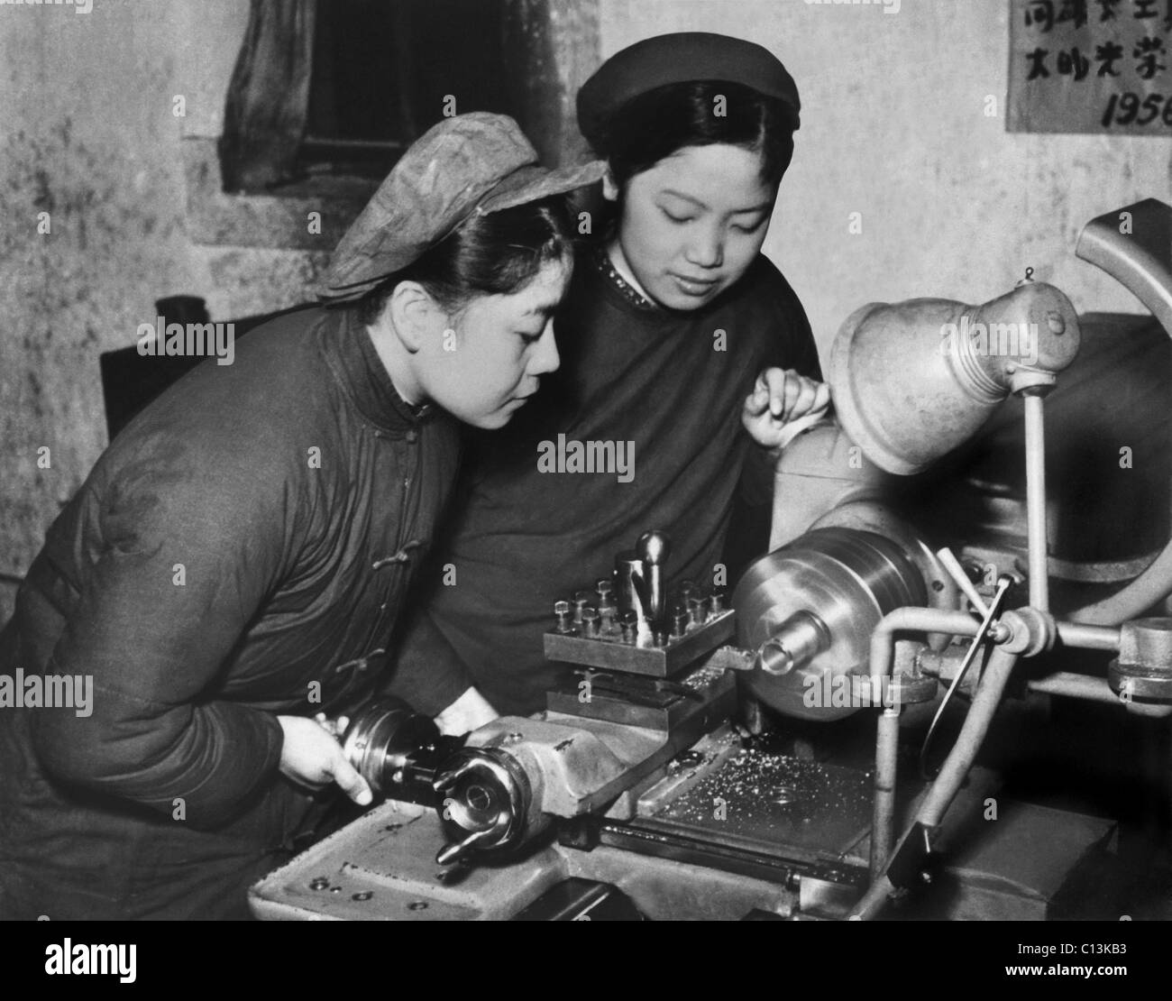 Two Chinese women in simple dark jackets, at their machines at a tool plant during the first decade of the People's Republic of Stock Photo