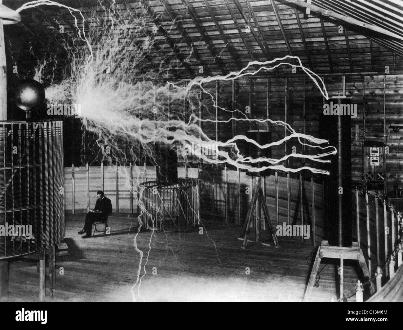 Nikola Tesla 1856-1943 created a double exposure photograph of himself reading undisturbed by a 22 foot long discharge of artificial lightning of millions of volts of electricity. Stock Photo