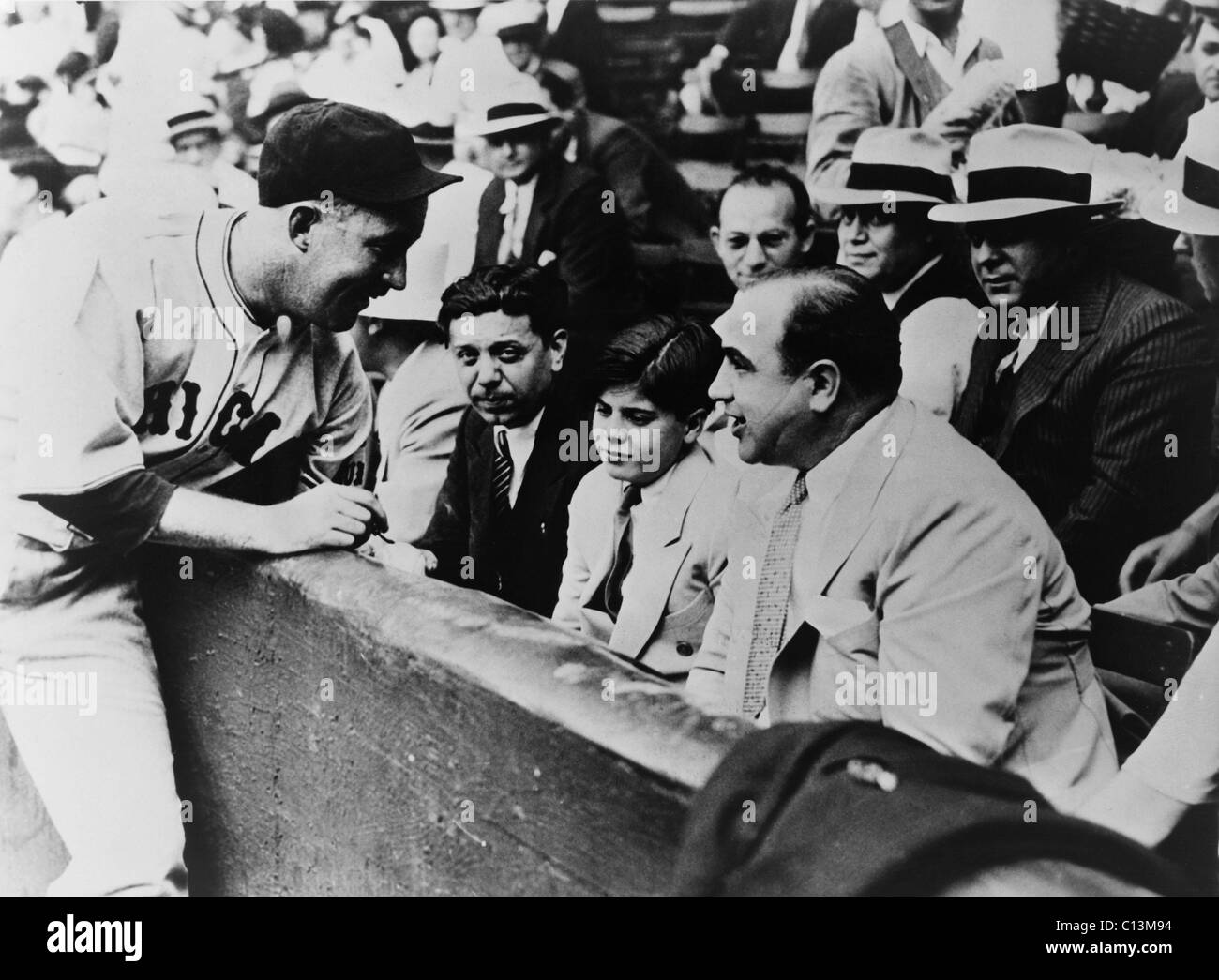 Chicago Cubs player Gabby Hartnett autographing a baseball for Sonny Capone who is sitting with his father Al Capone and other gangsters at a 1931 charity baseball game. Stock Photo