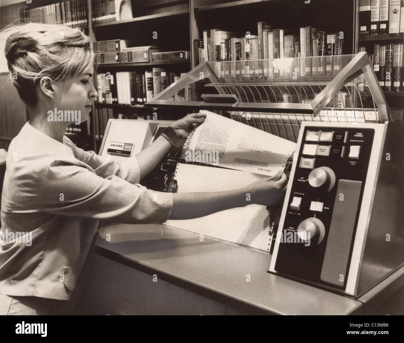 Librarian taking a printout from a UNIVAC 490 Printer. In the 1960s computer technology was available for specialists in this case to manage library catalogs and book circulation. 1966. Stock Photo