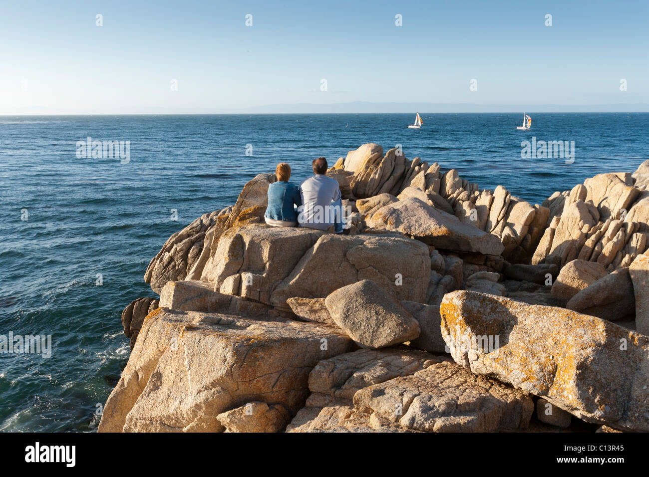 People sitting on rocks overlooking Monterey Bay in Pacific Grove, California Stock Photo