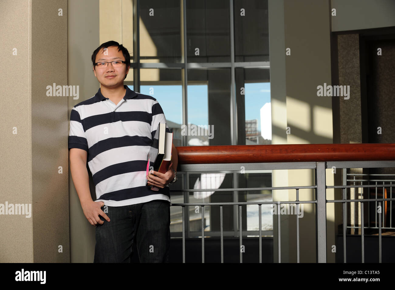 Portrait of smiling Asian student holding books indoors Stock Photo - Alamy