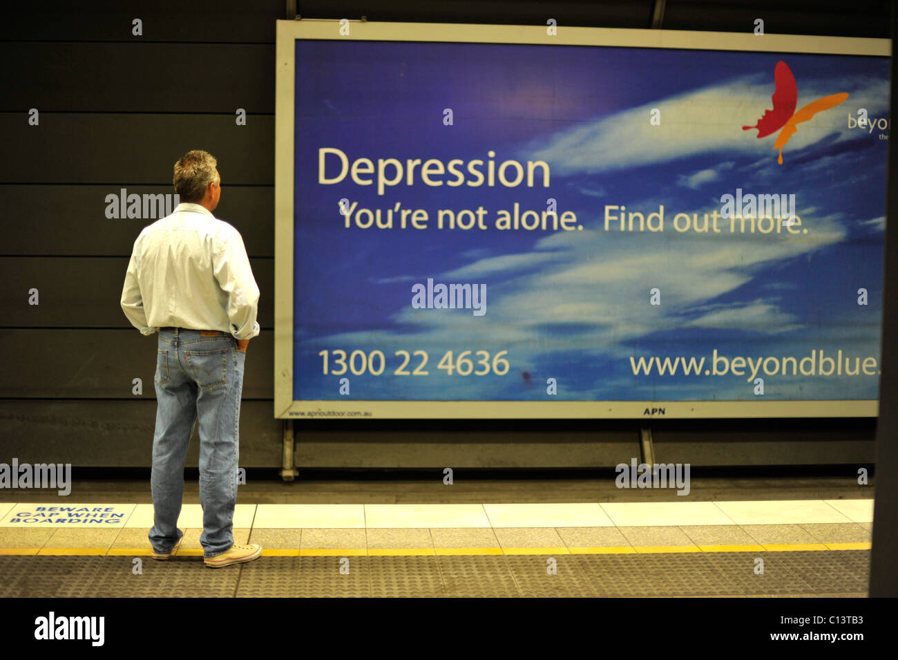 A man studies a poster advertising help for victims of depression in a railway station. Stock Photo