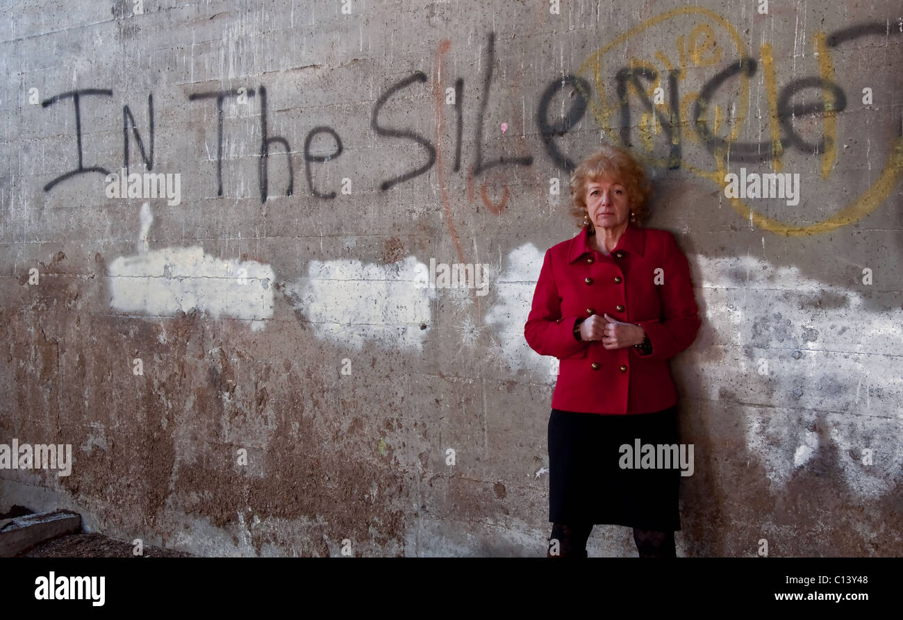This slightly haunting stock image how graffiti saying "In the Silence" on a cement wall, with a mature older Caucasian woman. Stock Photo