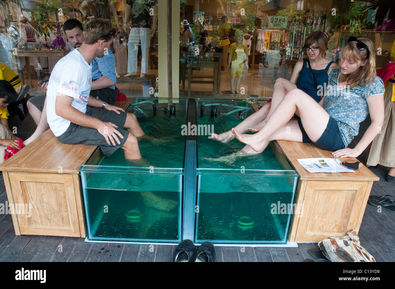 Tourists enjoying a fish spa where tiny fish nibble the dead skin from their feet in Ubud Bali Indonesia Stock Photo