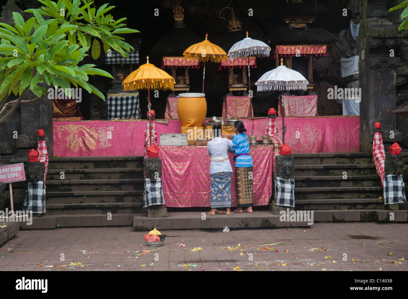 Two women make offerings at the altar in the 1000 year old bat cave temple called Pura Goa Lawah in Klungkung, Eastern Bali near Padang Bai Stock Photo