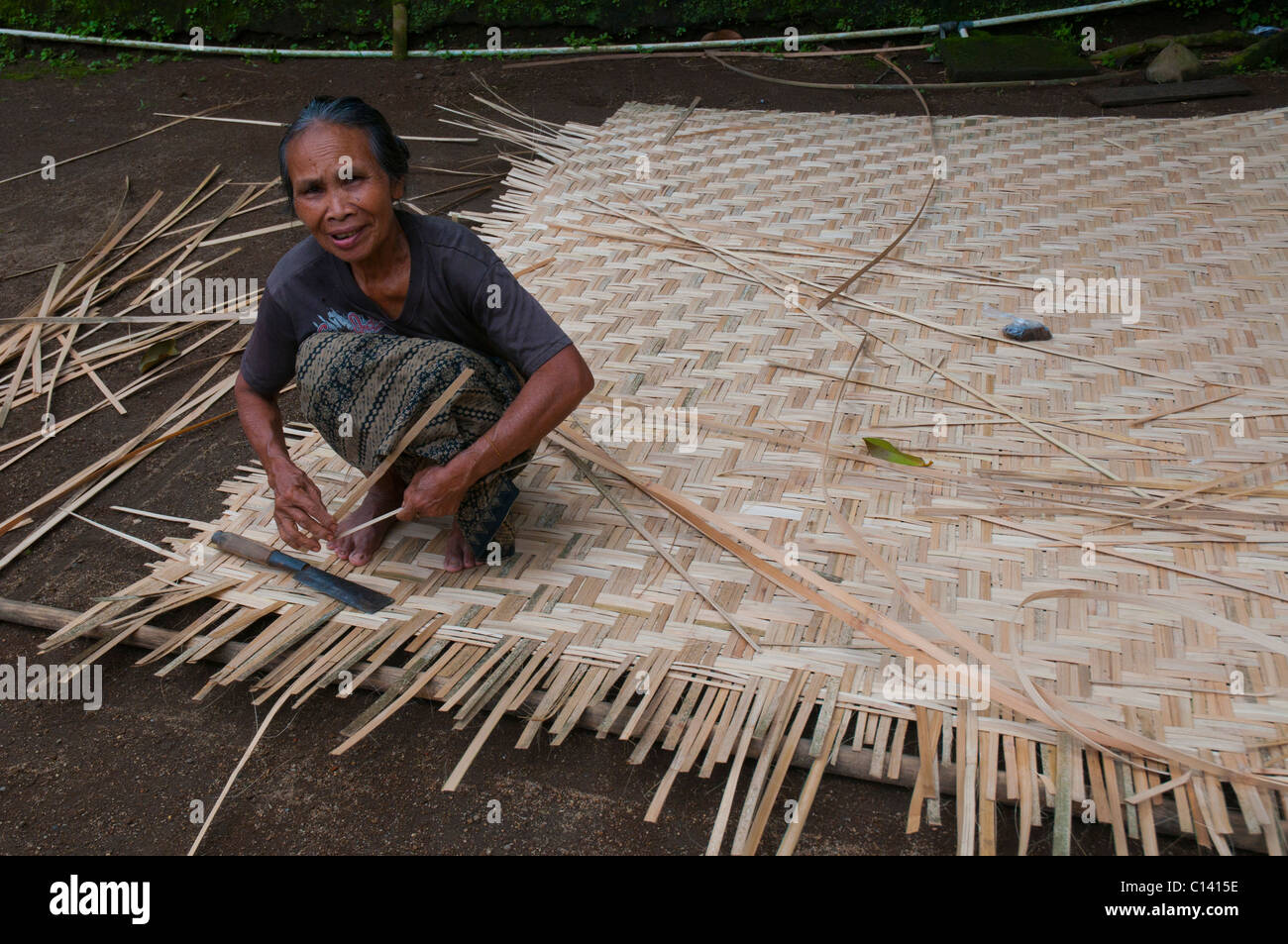 Woman weaving split bamboo into traditional panels for lining the walls
