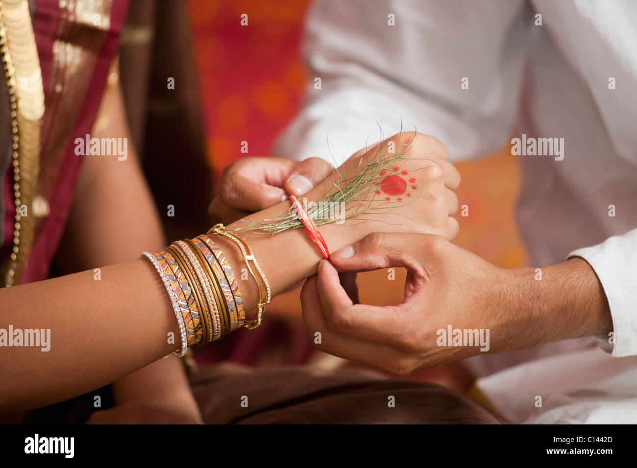 Close-up of a person's hands putting holy thread on a bride's wrist Stock Photo