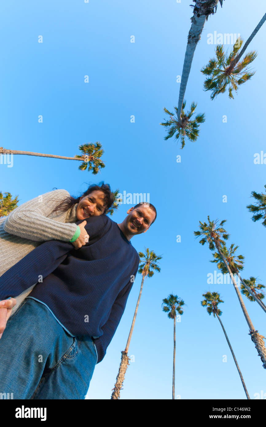 Couple hugging, looking at camera with sky and palm trees behind them.  Low angle POV.  Santa Barbara, California USA Stock Photo
