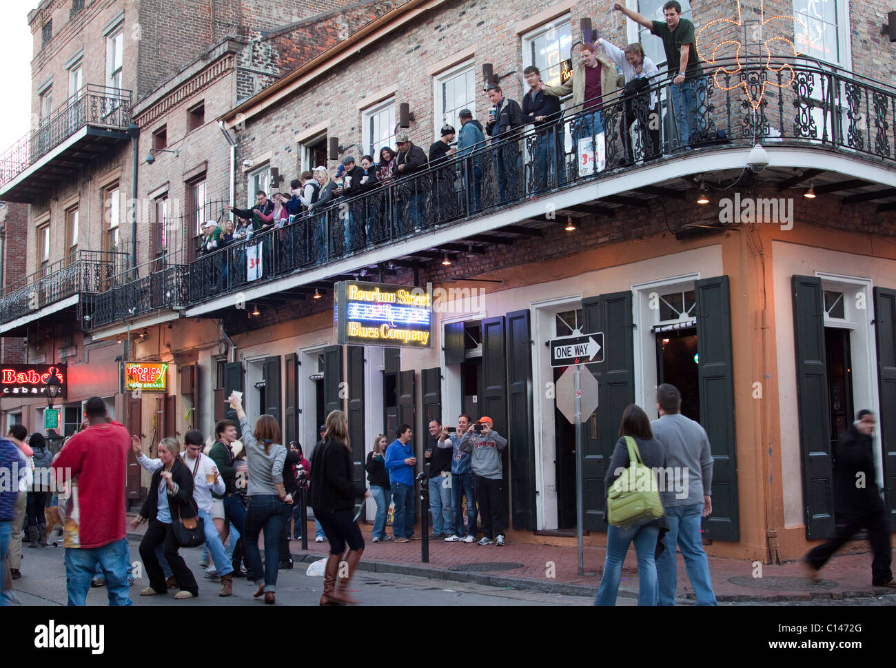 People drinking and dancing on the street as people watch on the balcony of a Bourbon Street bar in New Orleans Stock Photo