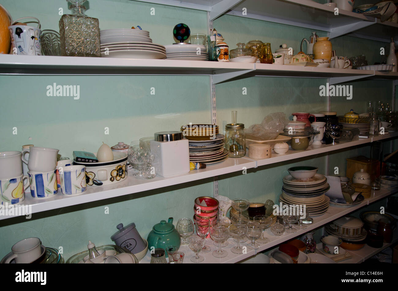 Shelves full of crockery and bric a brac in a charity shop Stock Photo