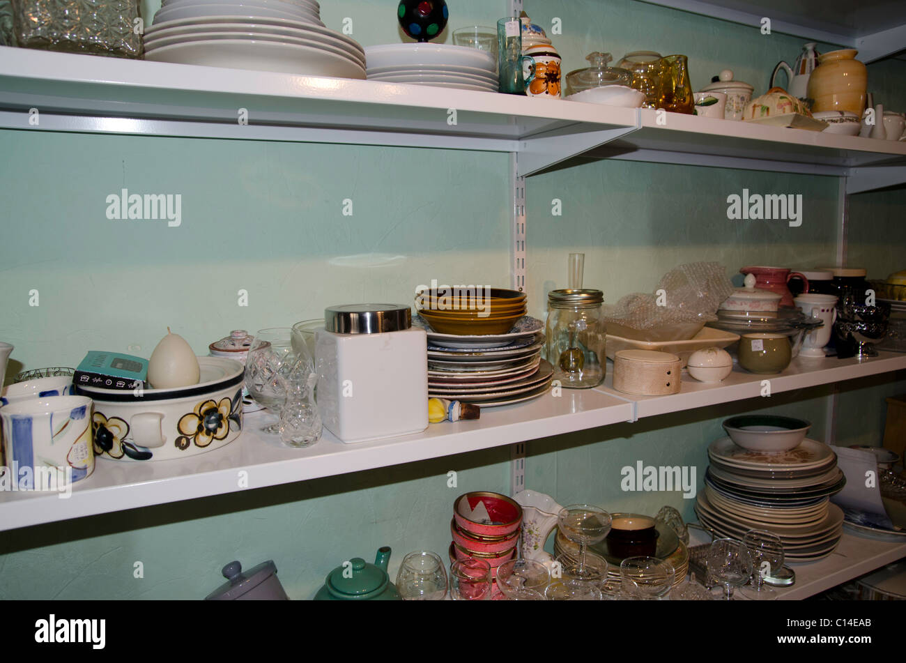 Shelves full of crockery and bric a brac in a charity shop Stock Photo
