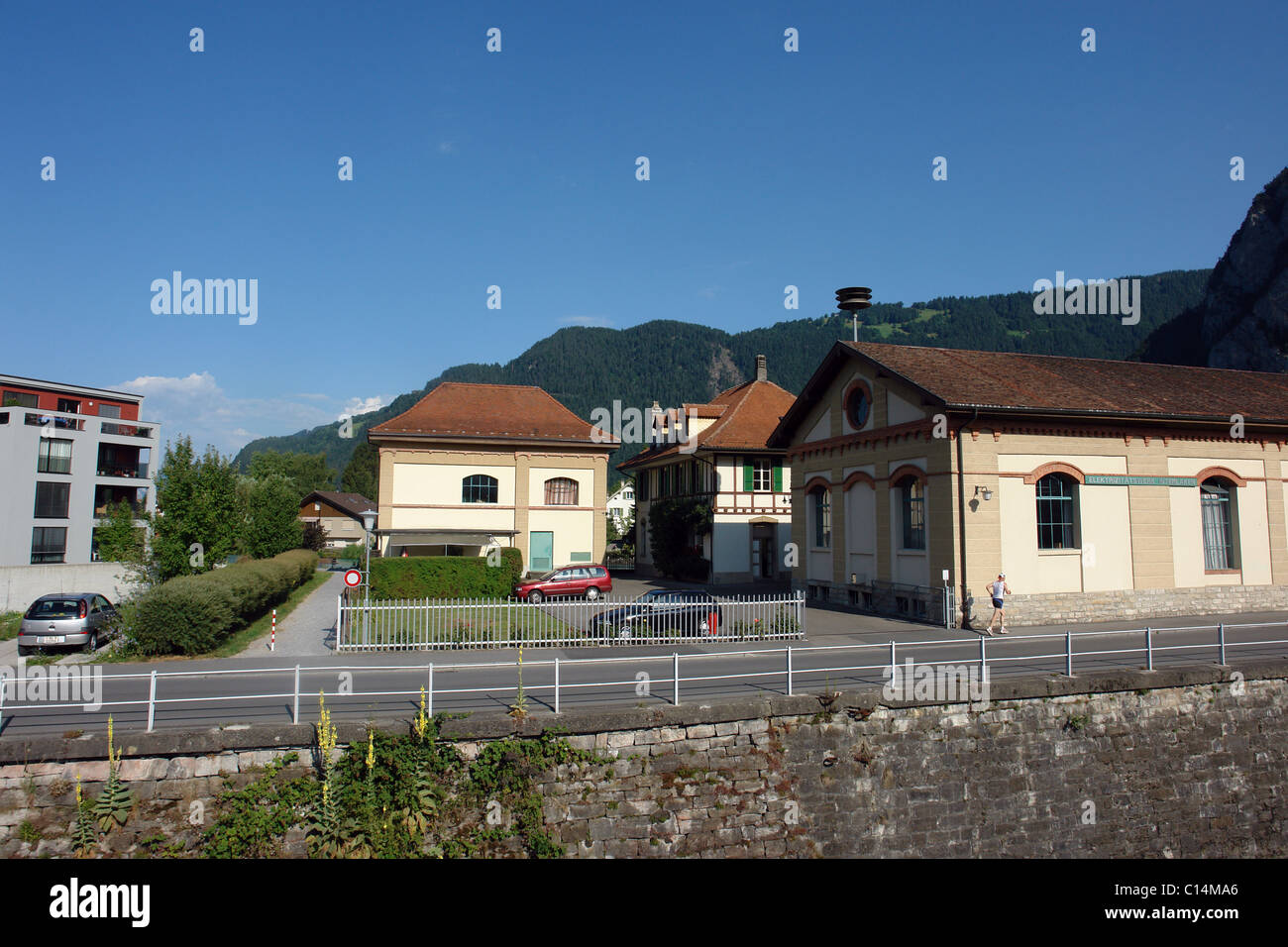 View of buildings in Interlaken next to the canal leading to lake Thun. In the background are hills covered with greenery. Stock Photo