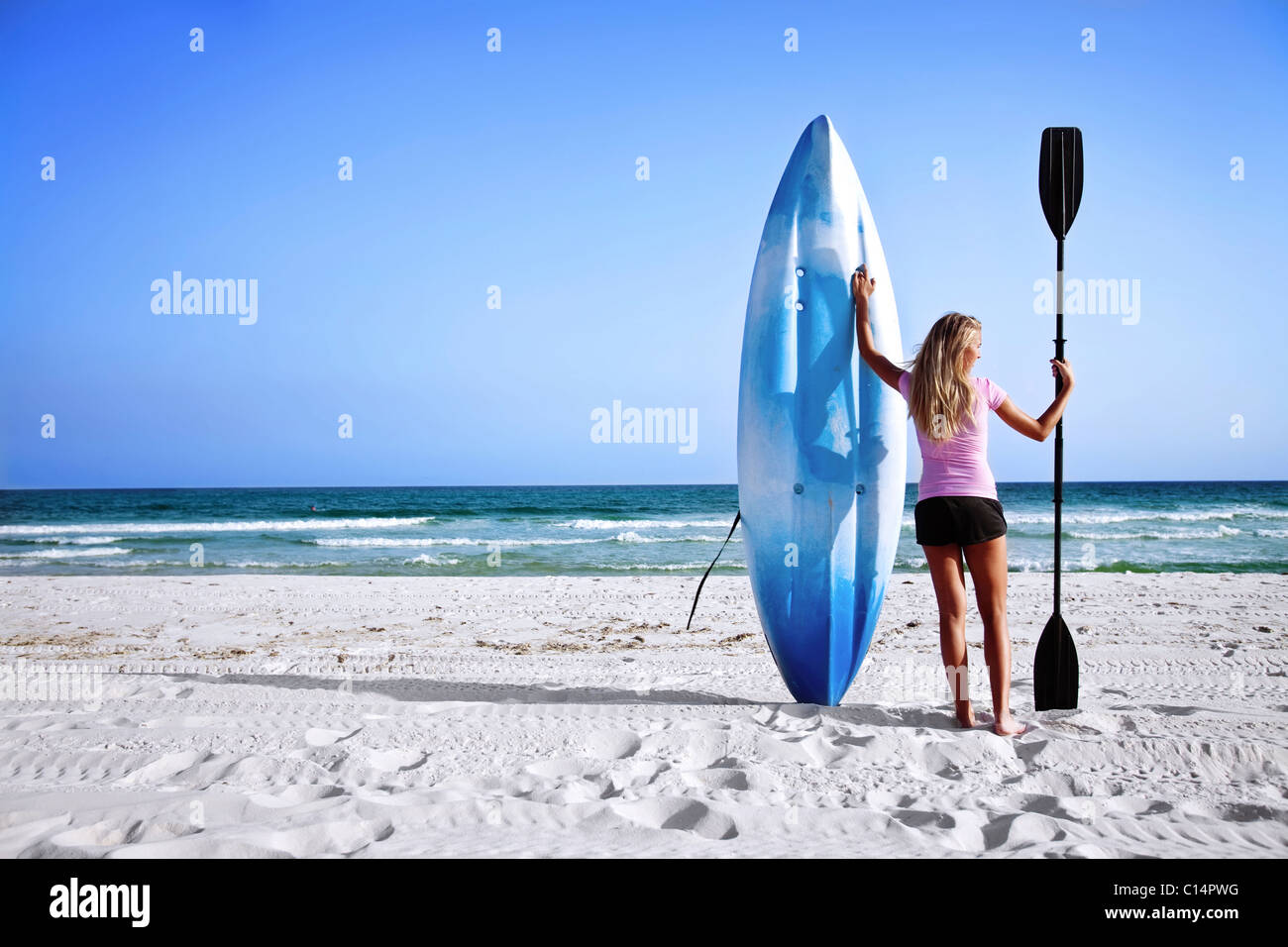 A girl holds up her sea kayak and paddle on Pensacola Beach, Florida. Stock Photo
