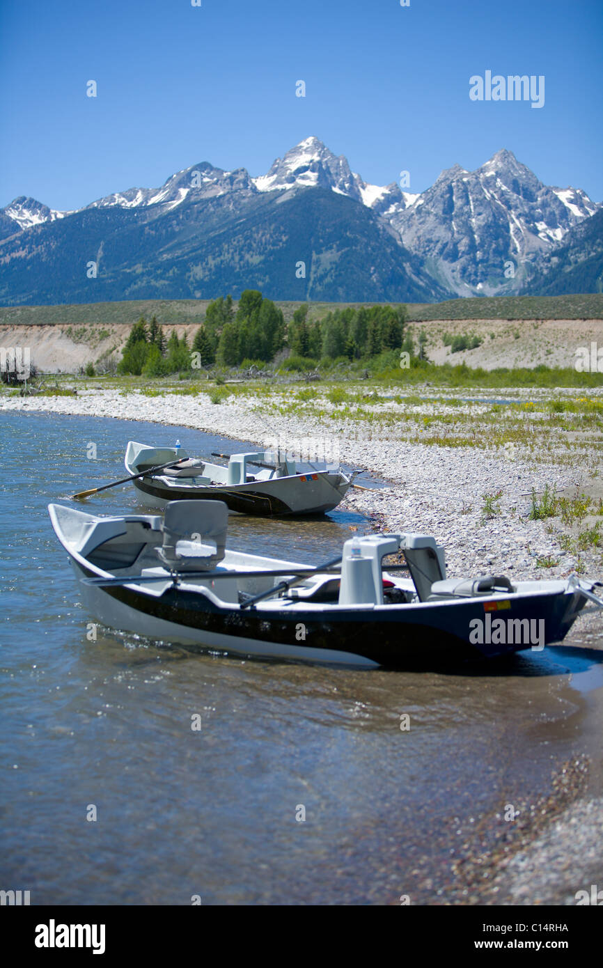Two river row boats sit on the shore of the Snake River with snow capped mountains in the background. Stock Photo