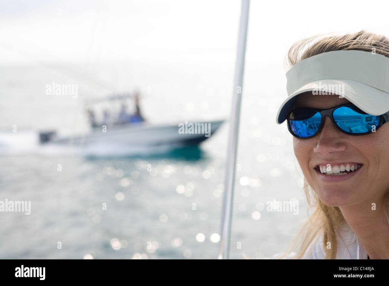 A mid adult woman on a boat is looking at the camera while a fishing boat crosses in the background. Stock Photo