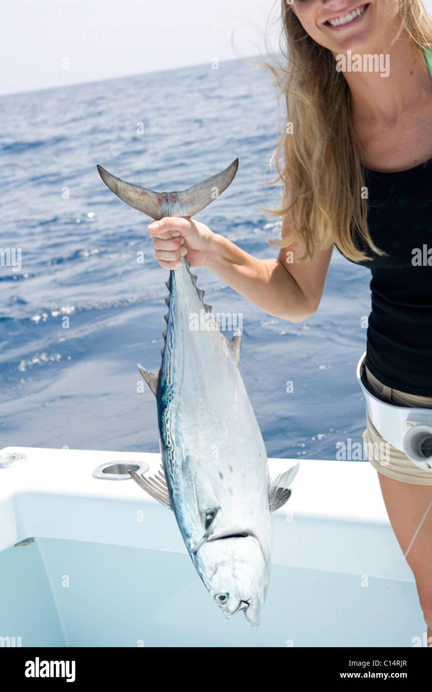 A mid adult blonde woman smiles as she holds up her freshly caught jack tuna. Stock Photo