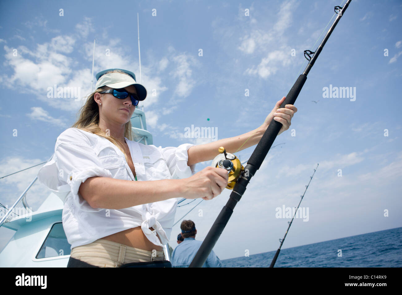 A blonde woman holds a fishing rod while watching for a sailfish to bite. Stock Photo