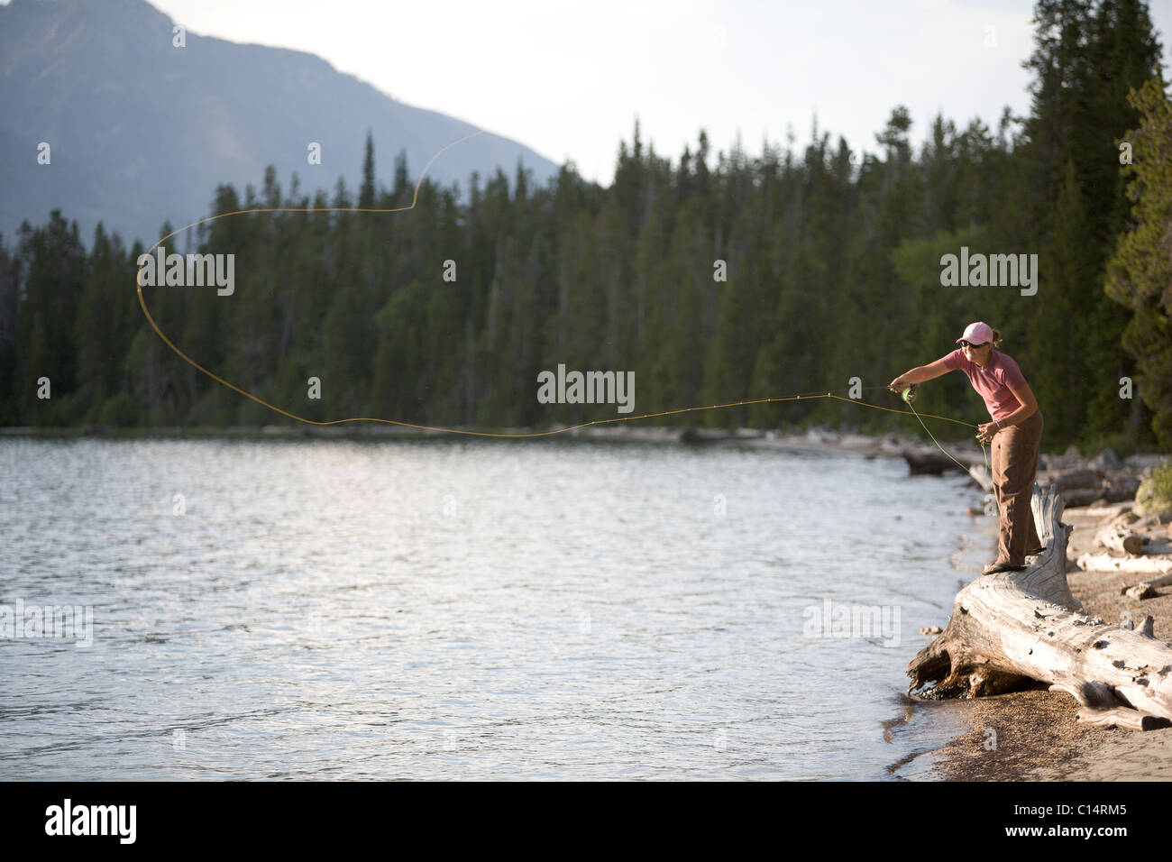 A woman casts her flyline from the shore of a lake. Stock Photo