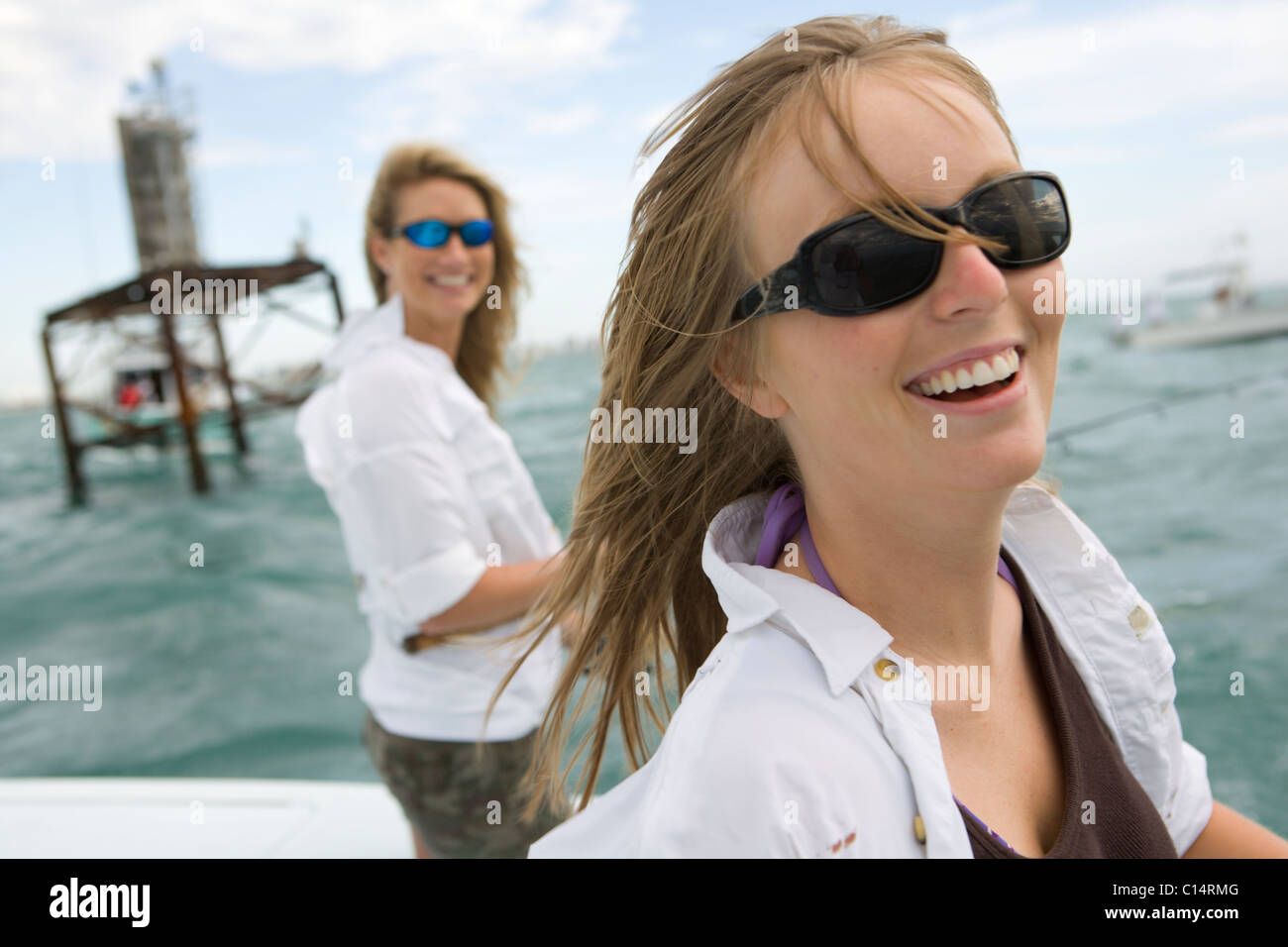 Two women are smiling at the camera with sunglasses while on a boat in the ocean. Stock Photo
