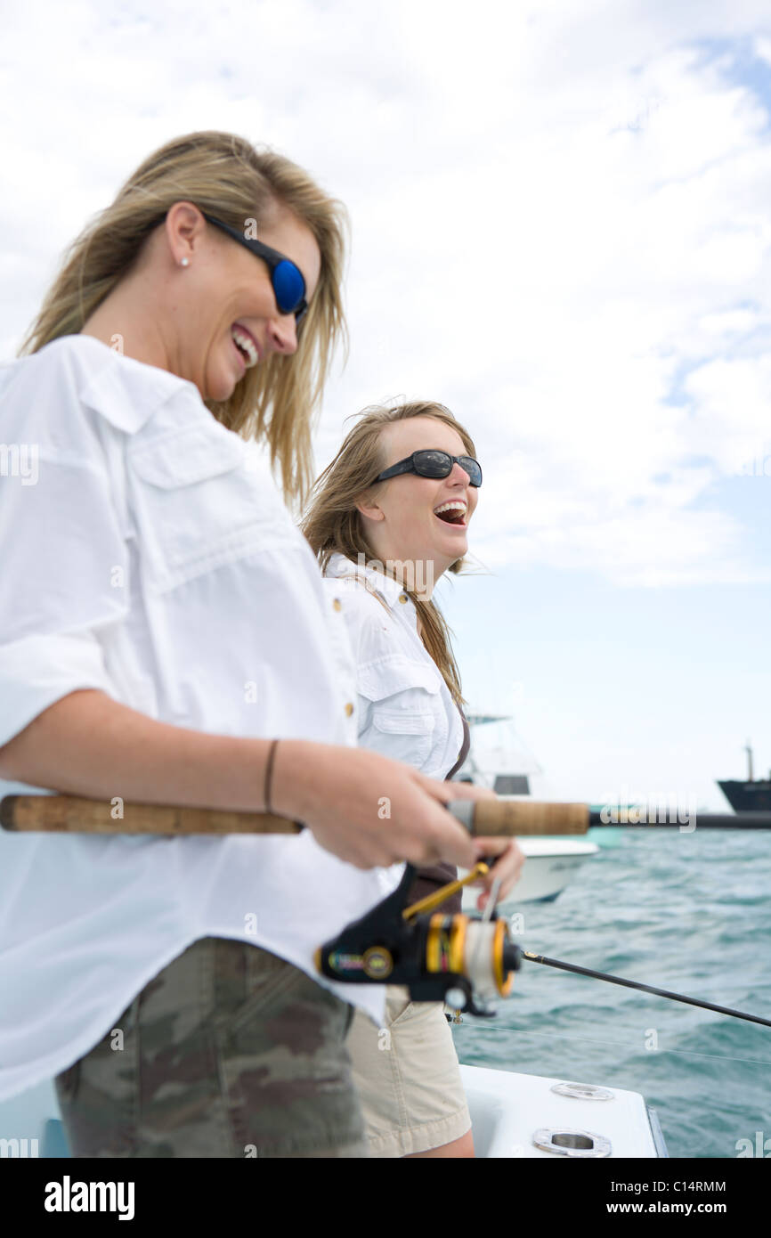 Two women are laughing while fishing off the side of a boat. Stock Photo