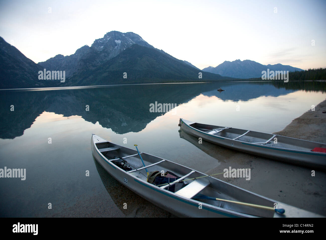 Two canoes at dusk are beached on the shore of Lake Leigh with the Grand Tetons in the distance. Stock Photo