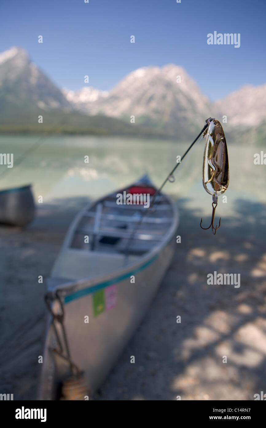 A close-up of a fishing lure with a canoe and mountains in the background. Stock Photo