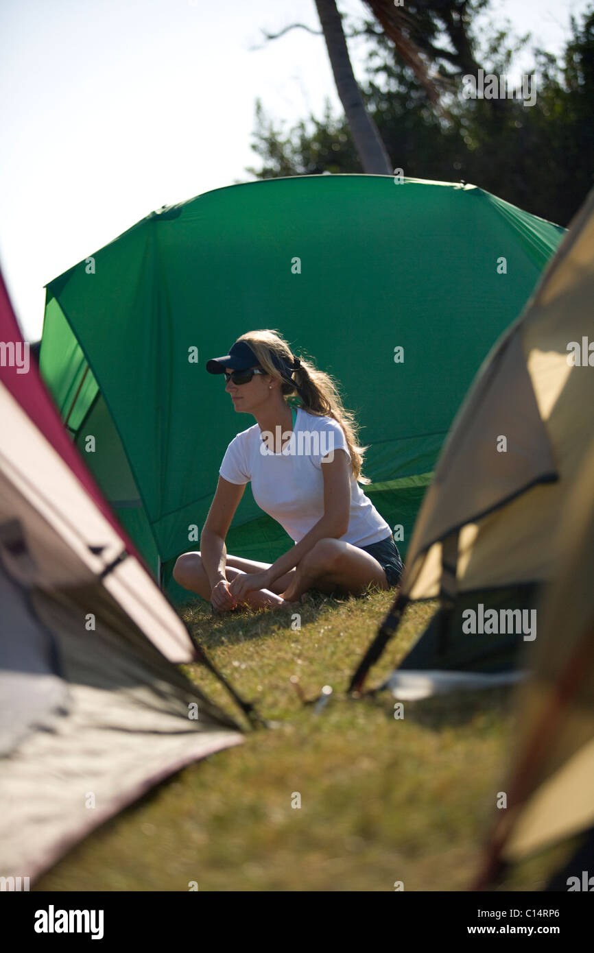 A blonde woman sits between tents at a campsite. Stock Photo