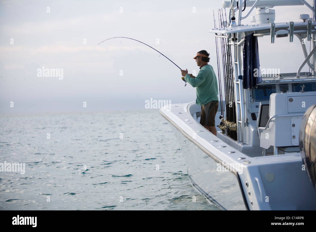 A fisherman reels in a catch off the side of his boat. Stock Photo