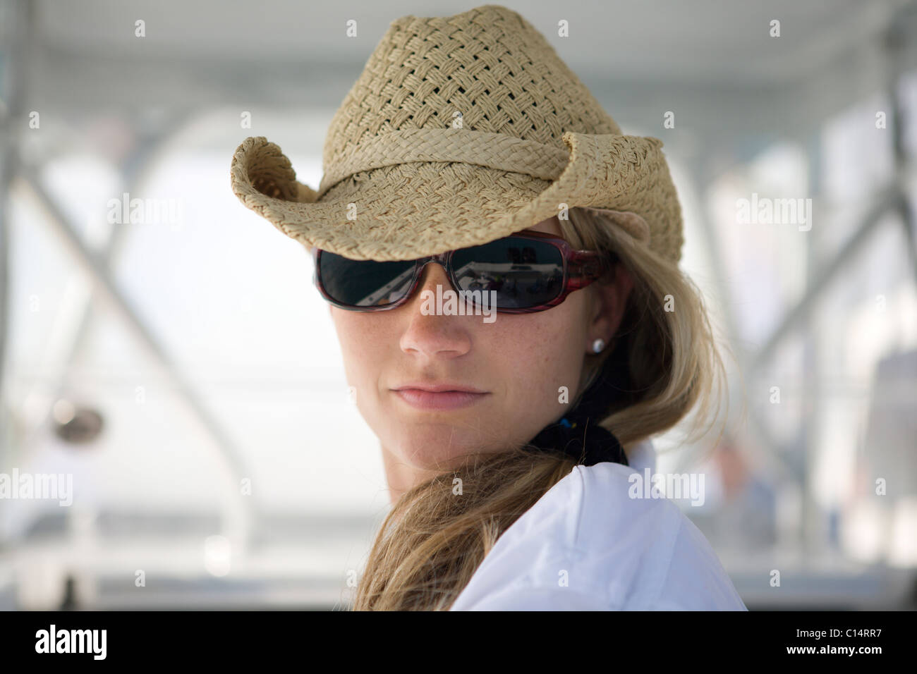 A close-up of a blonde woman as she looks at the camera wearing sunglasses and a straw hat. Stock Photo