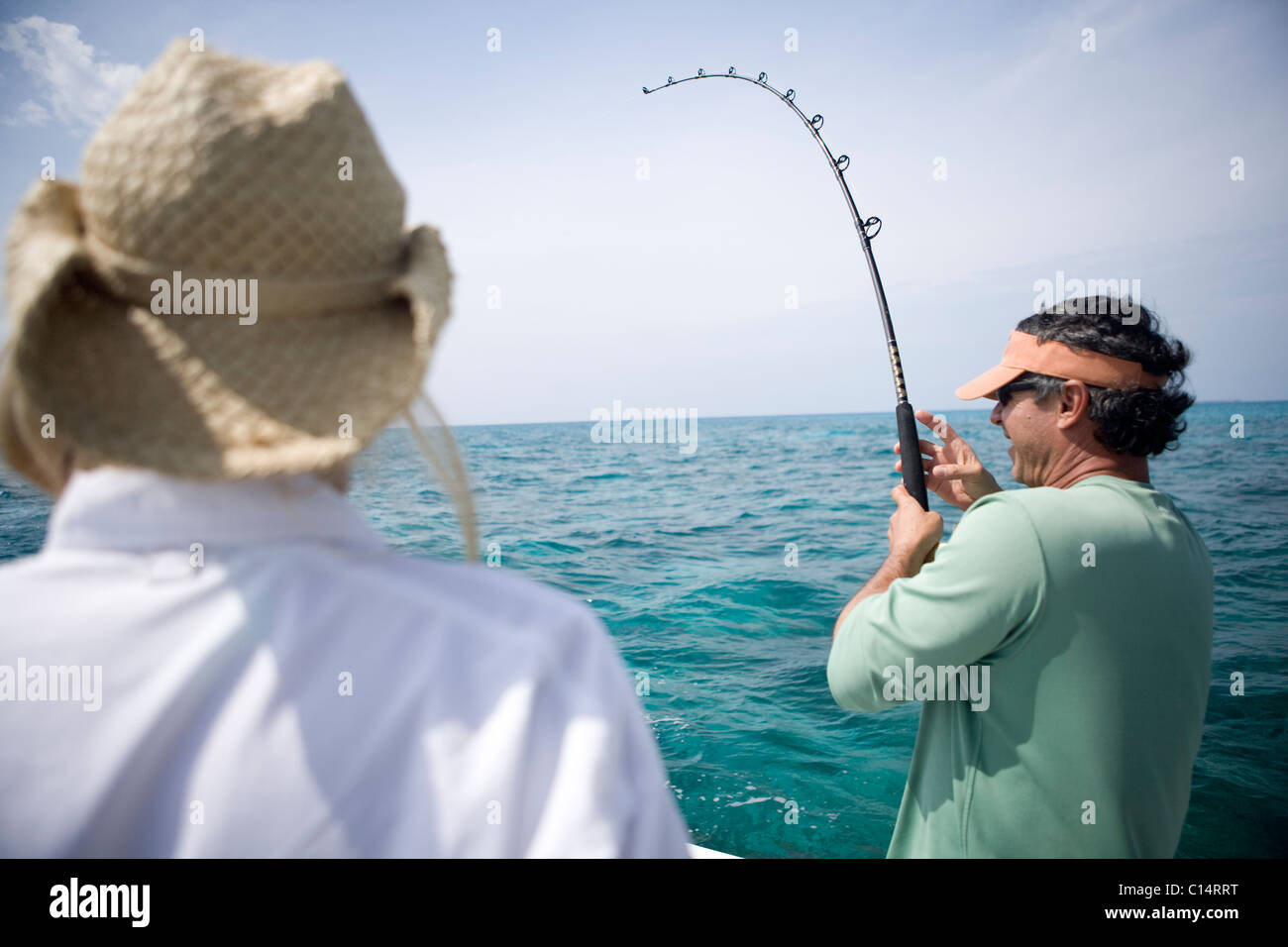 A fisherman reels in a fish as his pole bends down during the fight. Stock Photo