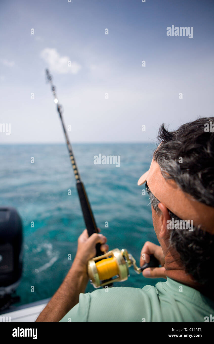 An over the shoulder view of a fisherman reeling in fish with blue water in the distance. Stock Photo
