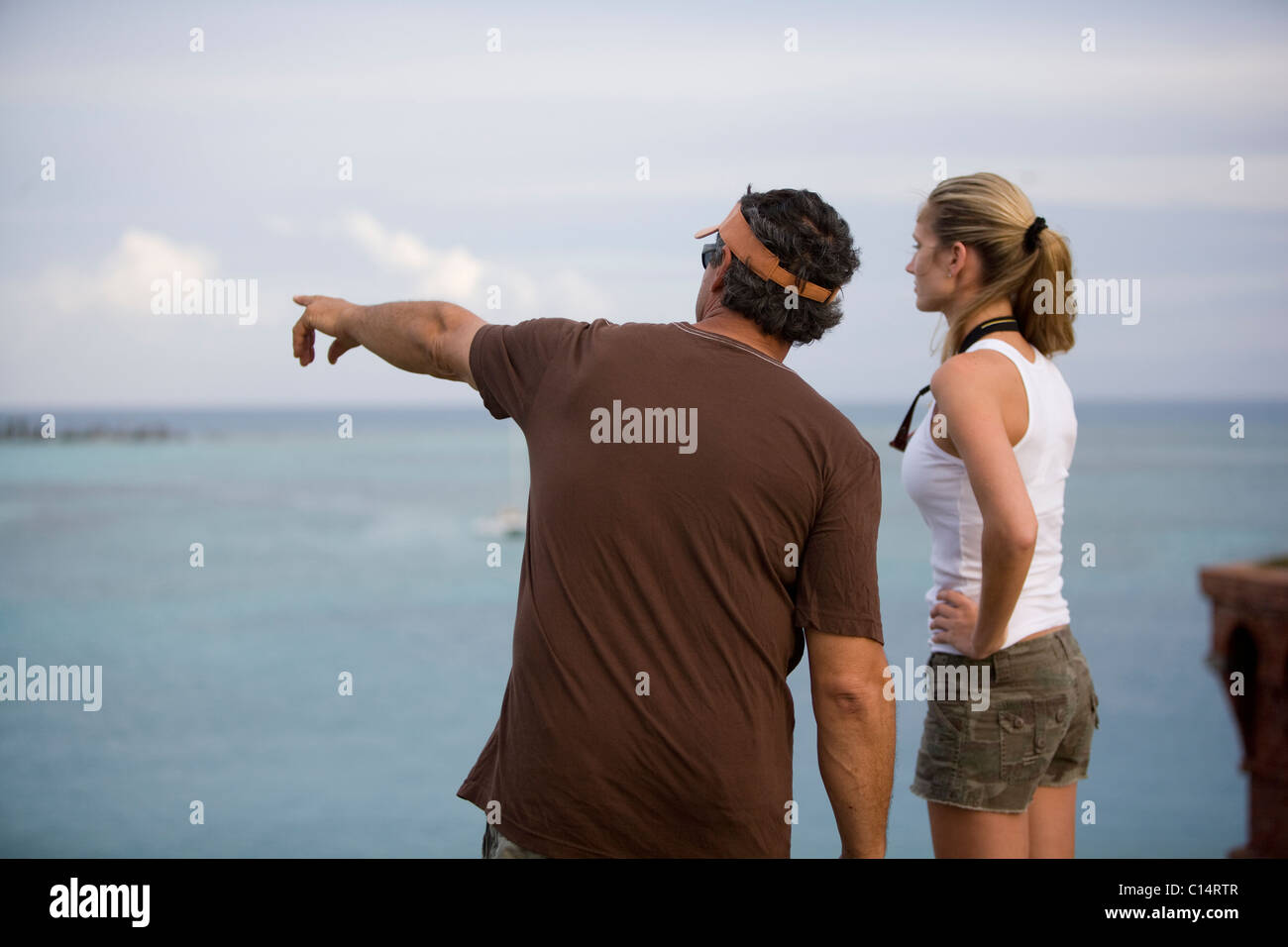 A man is pointing at something out in the distant blue water as a woman looks to see what it is. Stock Photo
